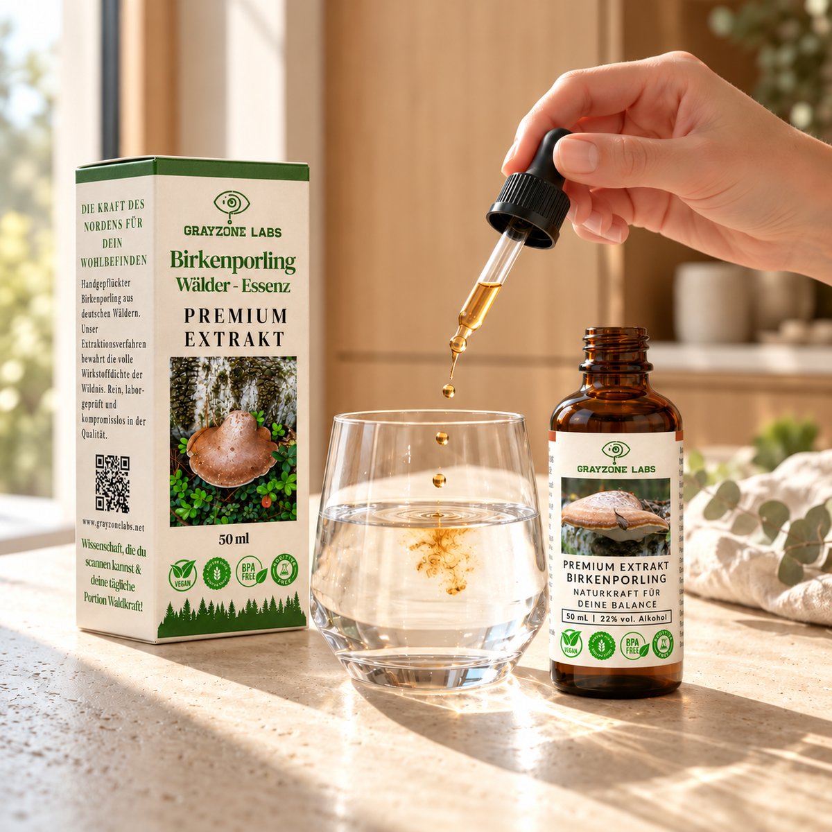 Birkenporling Tinktur wird mit der Pipette in ein Glas Wasser getropft, daneben Flasche und Faltschachtel von GrayZone Labs